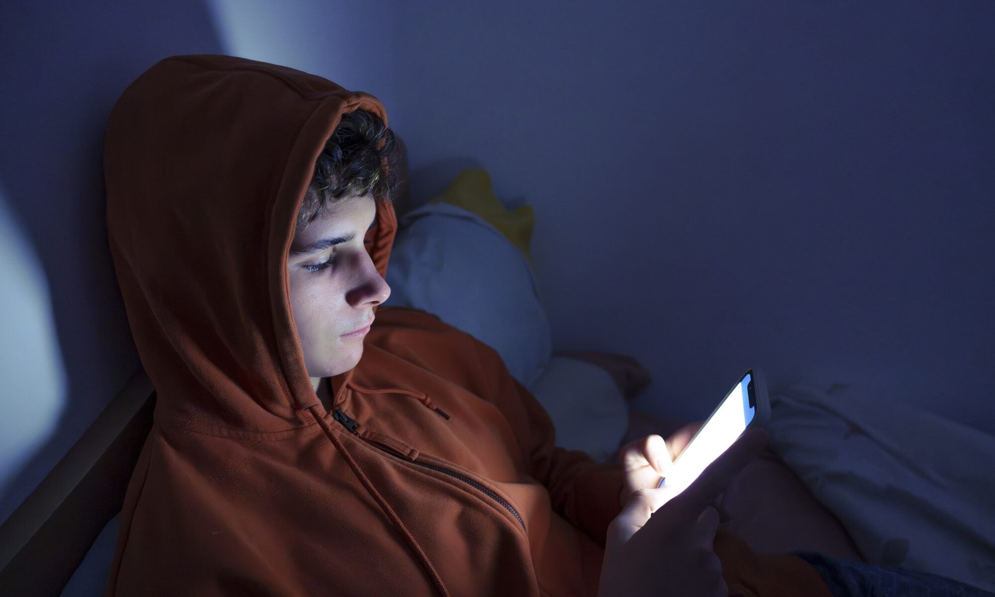 Teenager using a smartphone lying in bed late at night
